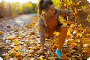 Mulher de meia-idade fazendo alongamento ou exercício de agachamento/avanço (lunge) em um caminho coberto por folhas de outono. A imagem simboliza treino, vitalidade e a manutenção da performance após os 40.